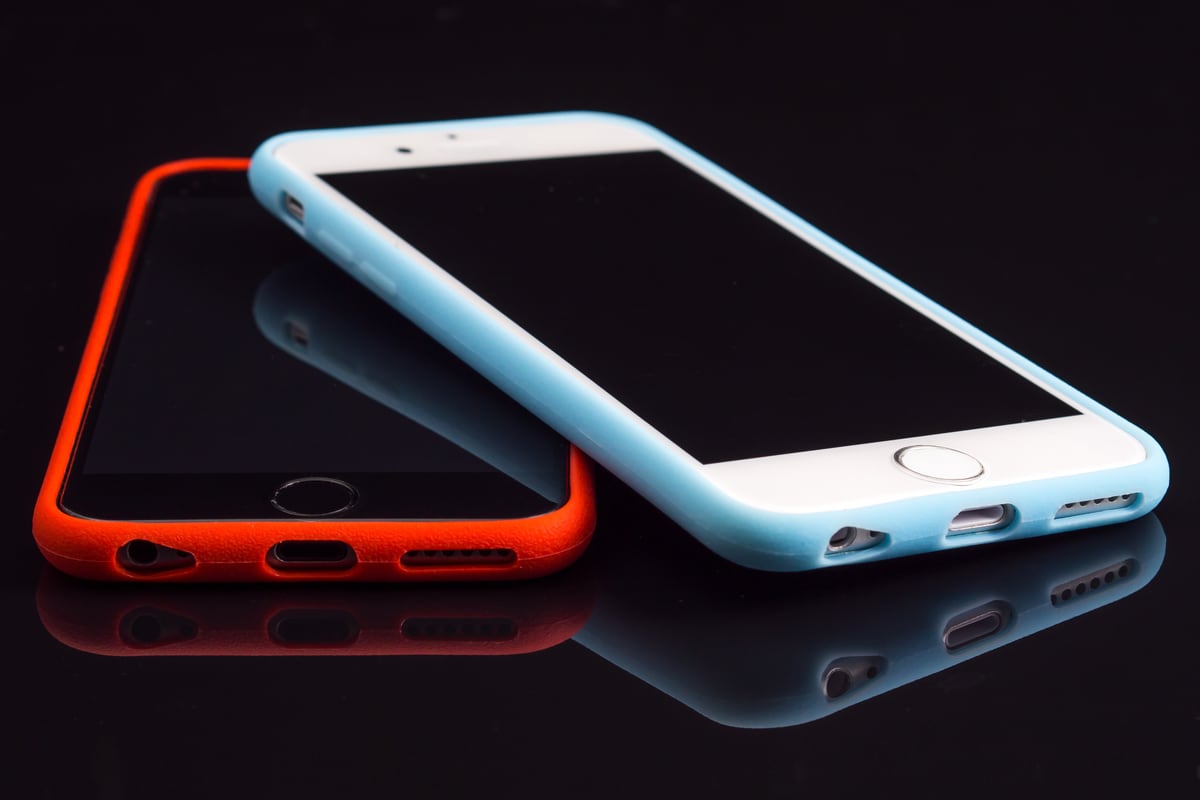 Two smartphones, one in an orange case, lying on a dark reflective surface