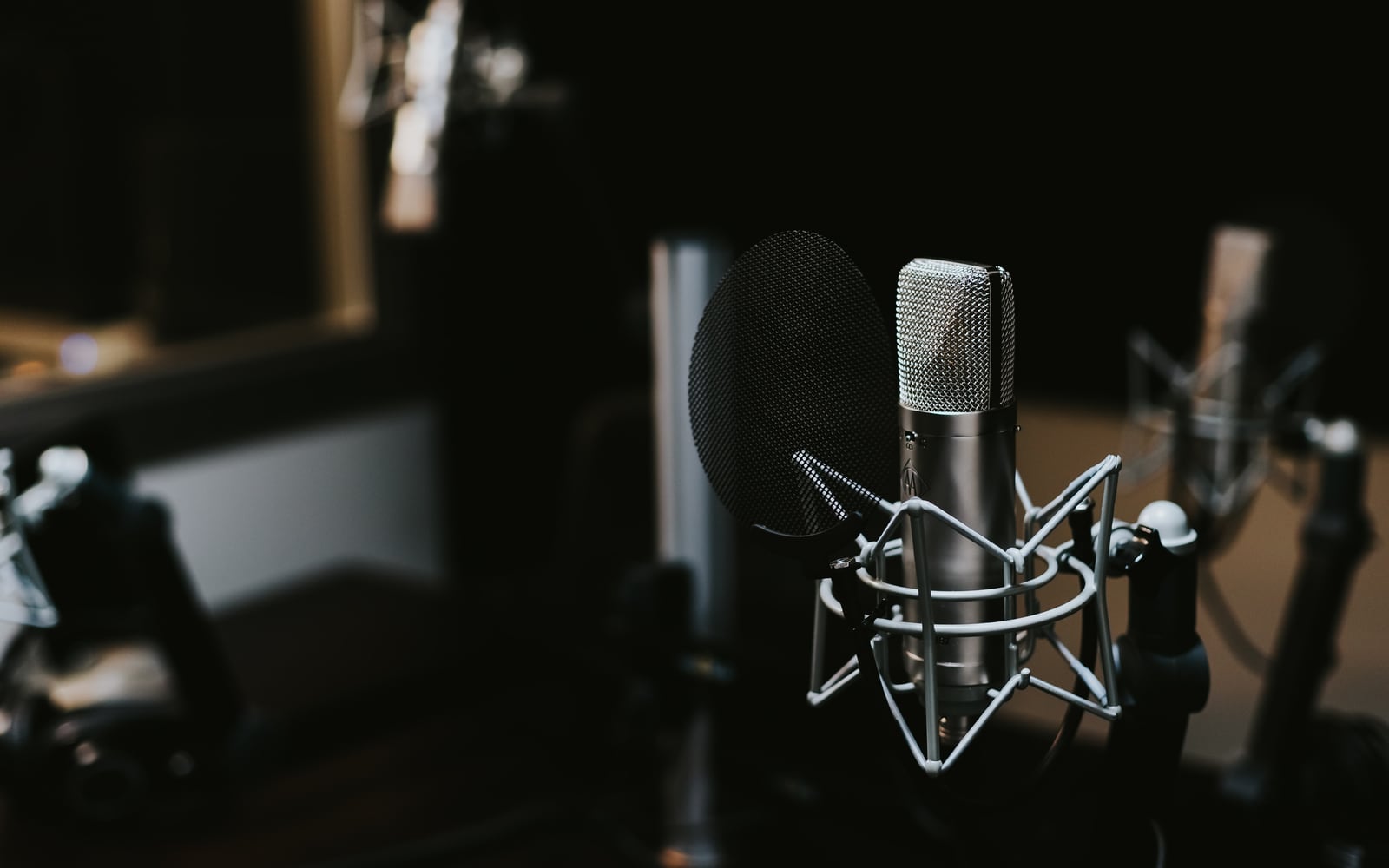 A silver studio microphone in a shock mount against a dark background